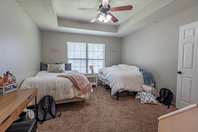 carpeted bedroom with a textured ceiling, ceiling fan, and a raised ceiling