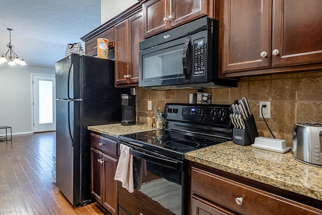 kitchen featuring black appliances, backsplash, decorative light fixtures, a notable chandelier, and light hardwood / wood-style flooring