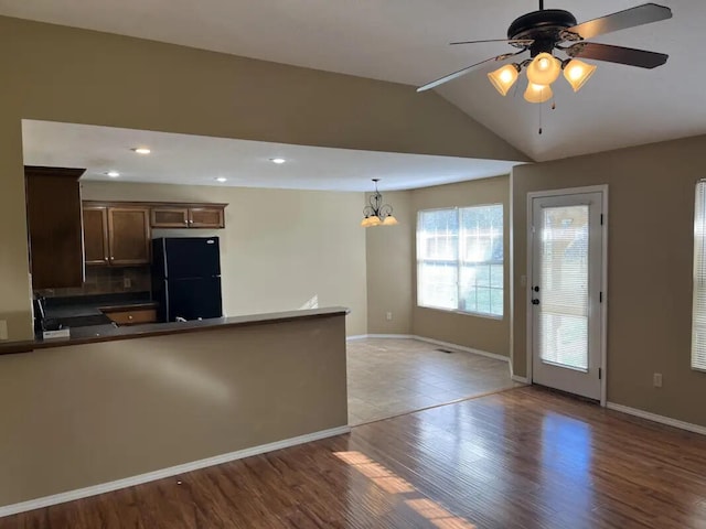 kitchen featuring ceiling fan with notable chandelier, light hardwood / wood-style floors, black fridge, vaulted ceiling, and decorative light fixtures