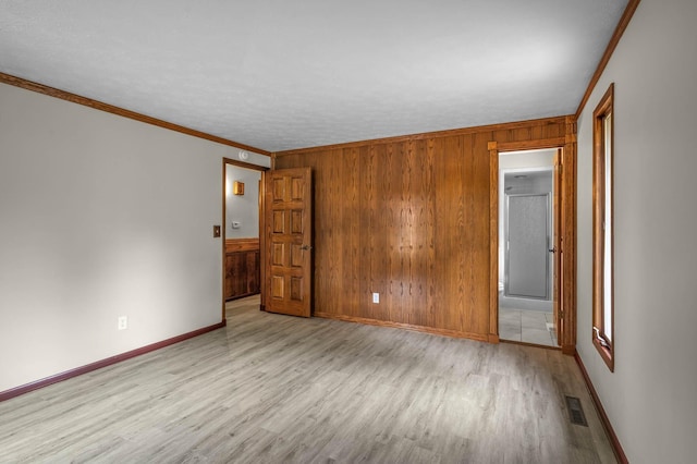 unfurnished room featuring light hardwood / wood-style flooring, wood walls, and crown molding