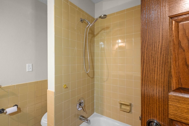 bathroom with tile walls, tiled shower / bath combo, and toilet