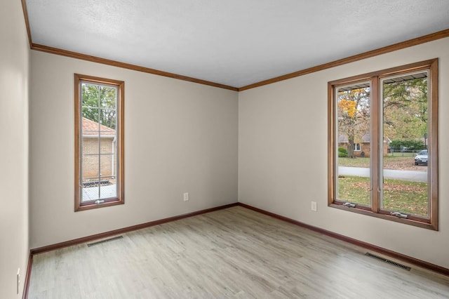 empty room featuring ornamental molding, light wood-type flooring, and a textured ceiling