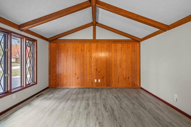 unfurnished living room featuring wood walls, lofted ceiling with beams, and wood-type flooring