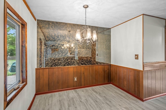 unfurnished dining area featuring ornamental molding, light wood-type flooring, a wealth of natural light, and a notable chandelier