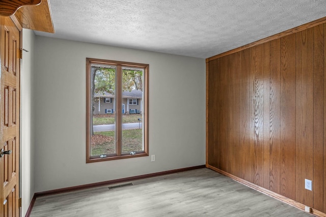 unfurnished room featuring wooden walls, a textured ceiling, and light hardwood / wood-style floors