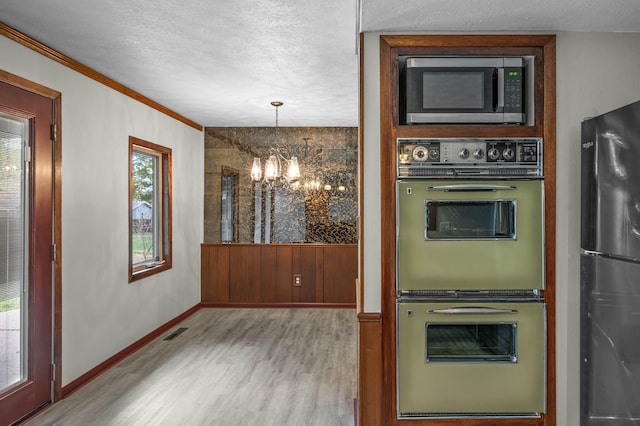 kitchen with appliances with stainless steel finishes, a textured ceiling, hardwood / wood-style floors, a chandelier, and pendant lighting