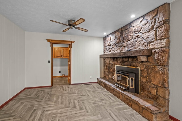 unfurnished living room featuring a wood stove, wood walls, a textured ceiling, ceiling fan, and light parquet flooring