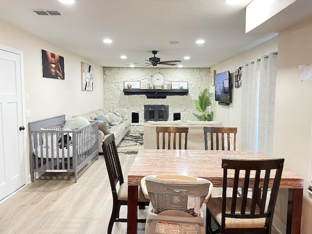 dining room featuring a stone fireplace, wood-type flooring, and ceiling fan