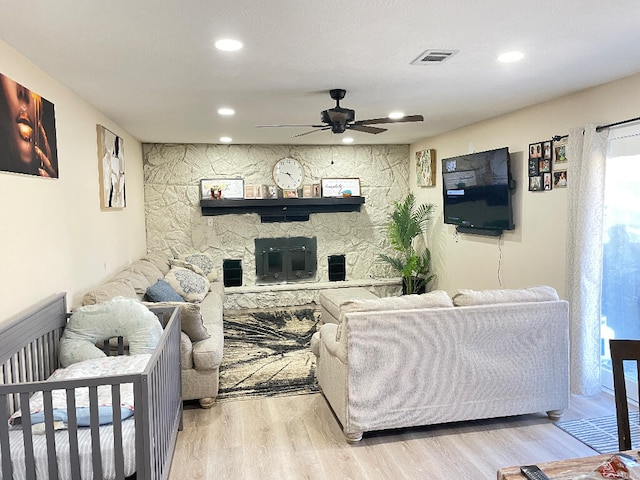 living room with a fireplace, ceiling fan, and light hardwood / wood-style flooring