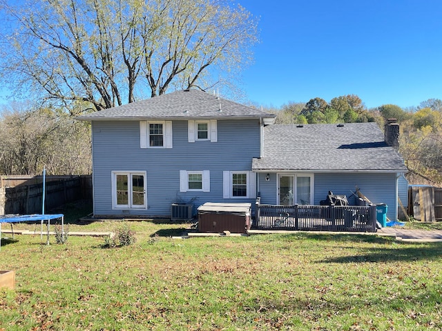 rear view of property featuring a hot tub, central AC, a trampoline, and a lawn