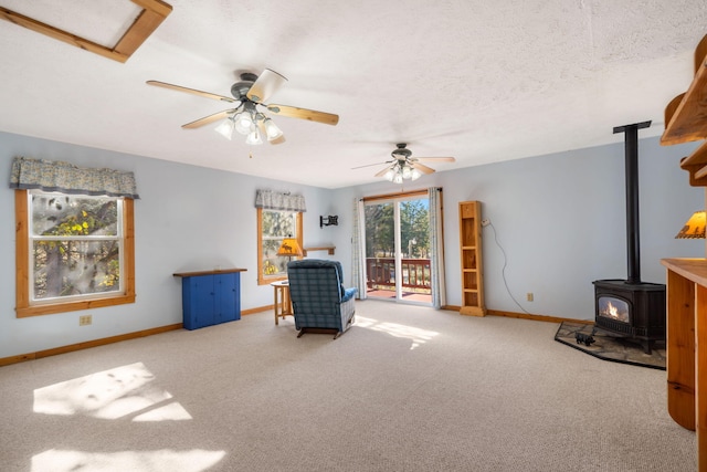 sitting room featuring ceiling fan, light colored carpet, a textured ceiling, and a wood stove