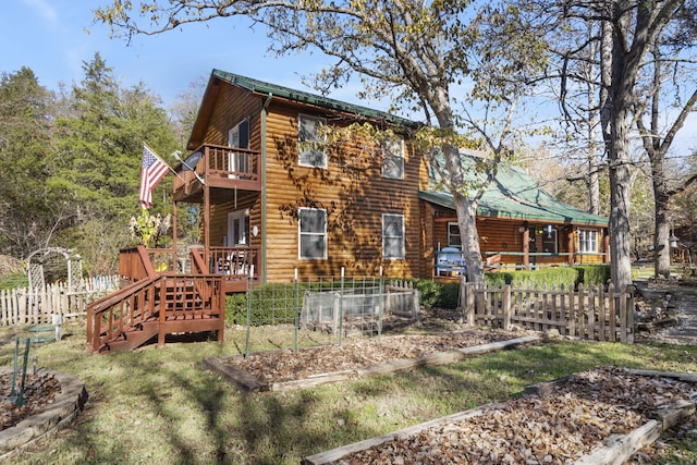view of front of property featuring a deck, faux log siding, a balcony, and fence