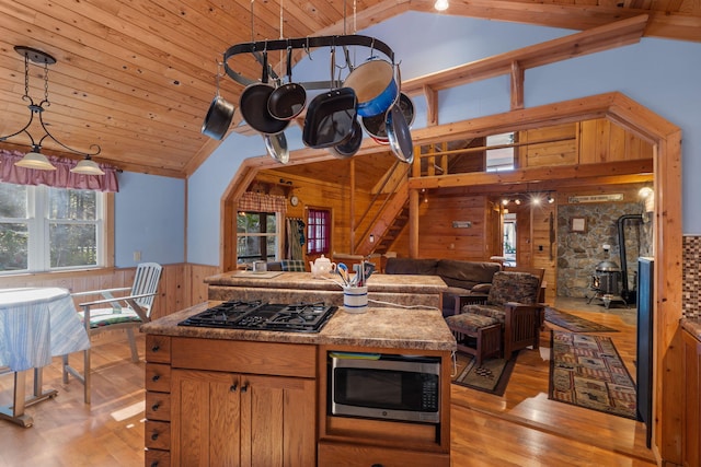 kitchen with wood ceiling, a wood stove, hanging light fixtures, black gas cooktop, and wood walls