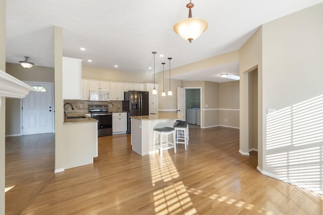 kitchen with light hardwood / wood-style floors, a center island, black appliances, sink, and white cabinetry