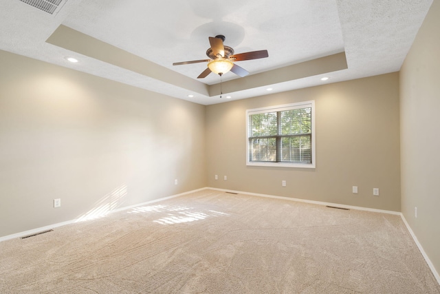 empty room with a textured ceiling, light colored carpet, ceiling fan, and a raised ceiling