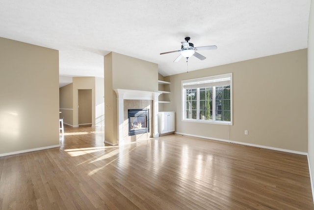 unfurnished living room with a tiled fireplace, ceiling fan, a textured ceiling, light wood-type flooring, and vaulted ceiling