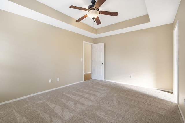 carpeted spare room with ceiling fan and a tray ceiling