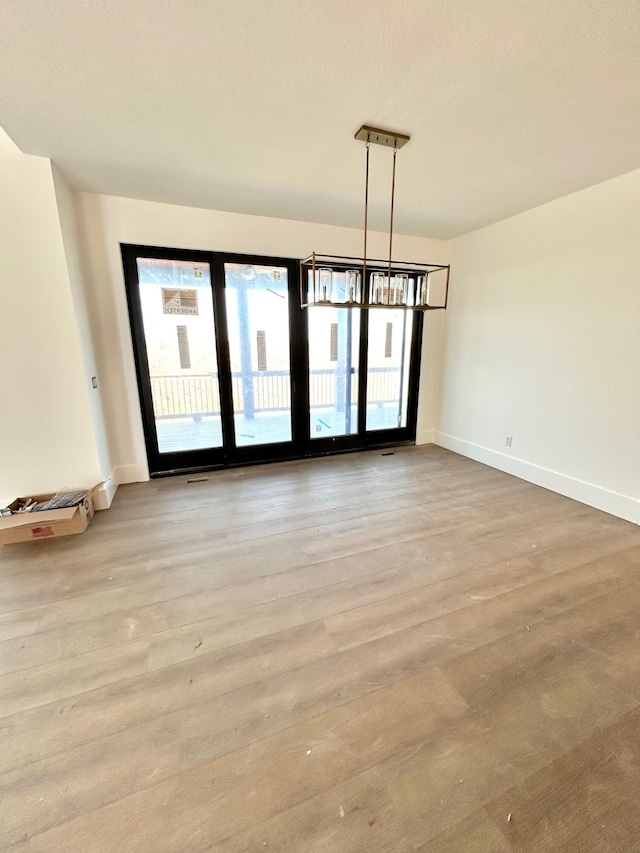 spare room with light wood-type flooring and an inviting chandelier