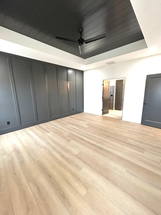 unfurnished room featuring a tray ceiling, ceiling fan, and light hardwood / wood-style flooring