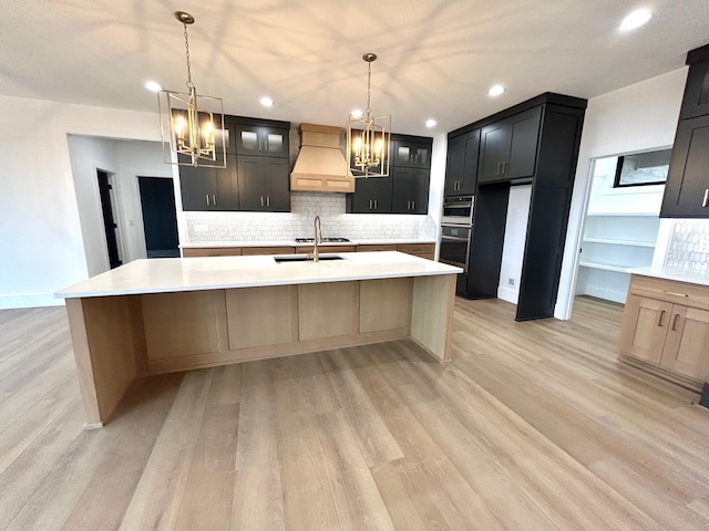 kitchen featuring sink, light brown cabinets, tasteful backsplash, premium range hood, and a center island with sink