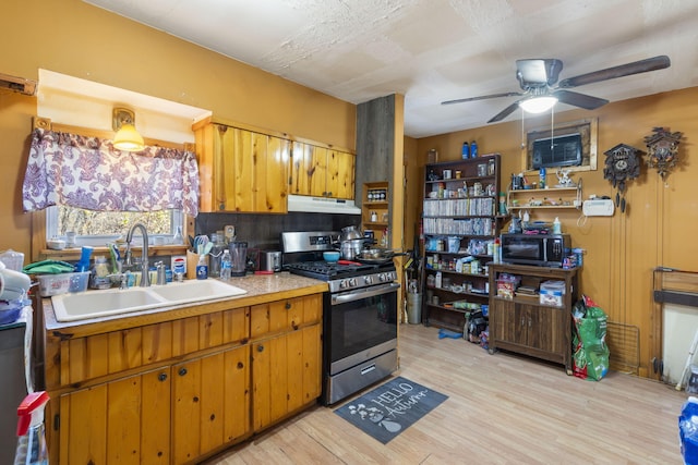 kitchen with stainless steel gas range, sink, light wood-type flooring, ceiling fan, and backsplash