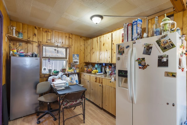 kitchen featuring stainless steel refrigerator, white refrigerator with ice dispenser, light hardwood / wood-style flooring, and wood walls