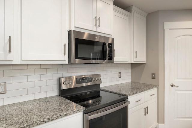 kitchen with tasteful backsplash, appliances with stainless steel finishes, light stone countertops, and white cabinets