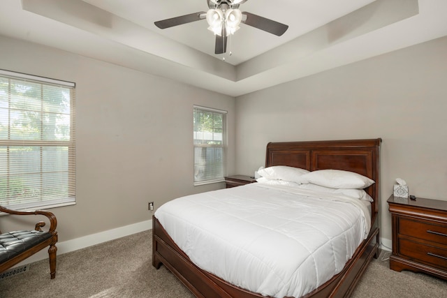 carpeted bedroom with a raised ceiling and ceiling fan