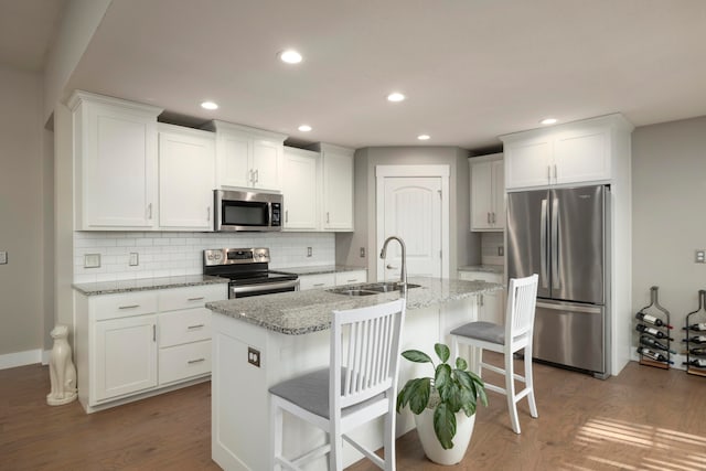 kitchen featuring a breakfast bar, sink, stainless steel appliances, light stone countertops, and a center island with sink