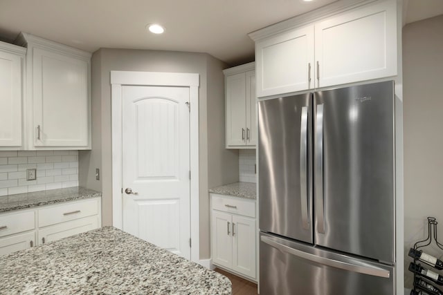 kitchen featuring tasteful backsplash, white cabinetry, light stone counters, and stainless steel refrigerator