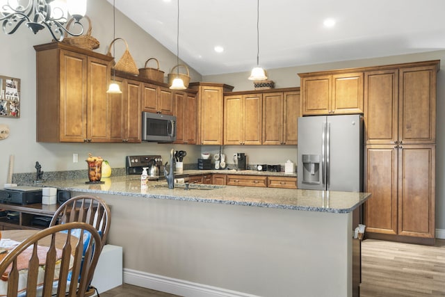 kitchen featuring kitchen peninsula, appliances with stainless steel finishes, light stone counters, vaulted ceiling, and light hardwood / wood-style floors