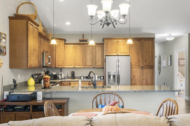 kitchen featuring light stone countertops, light wood-type flooring, decorative light fixtures, and appliances with stainless steel finishes