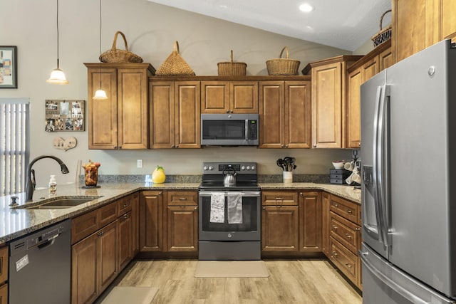 kitchen with pendant lighting, lofted ceiling, sink, appliances with stainless steel finishes, and light hardwood / wood-style floors