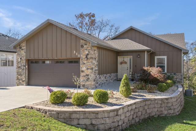 ranch-style home featuring a shingled roof, concrete driveway, a garage, stone siding, and board and batten siding