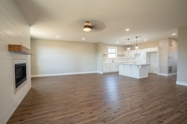 unfurnished living room featuring a fireplace, ceiling fan, sink, and dark hardwood / wood-style flooring