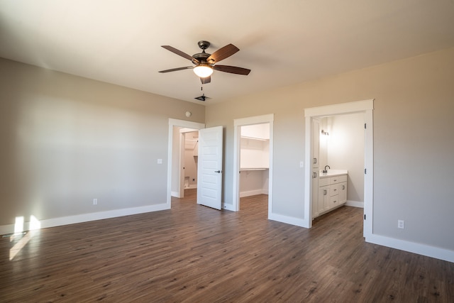 unfurnished bedroom featuring a closet, a walk in closet, ensuite bath, dark wood-type flooring, and ceiling fan