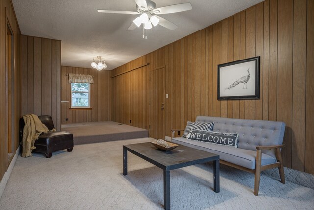 living room featuring a textured ceiling, ceiling fan with notable chandelier, light colored carpet, and wooden walls