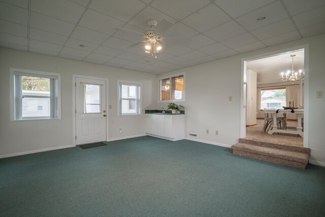 unfurnished living room with carpet, ceiling fan with notable chandelier, and a drop ceiling