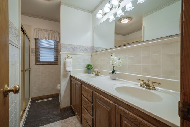 bathroom featuring vanity, toilet, a shower with shower door, and tile walls