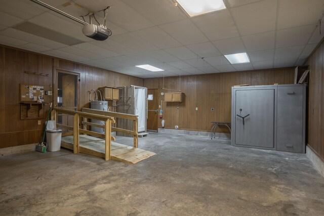 basement with a paneled ceiling, water heater, and wood walls