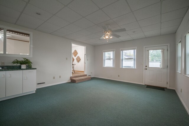 unfurnished living room featuring carpet flooring, ceiling fan, and a drop ceiling