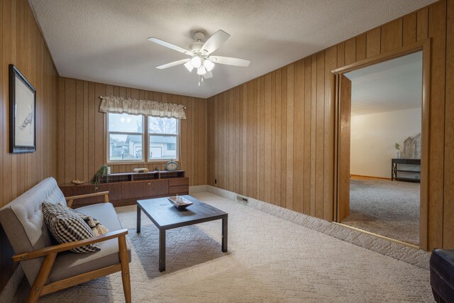 carpeted living room featuring ceiling fan, wood walls, and a textured ceiling