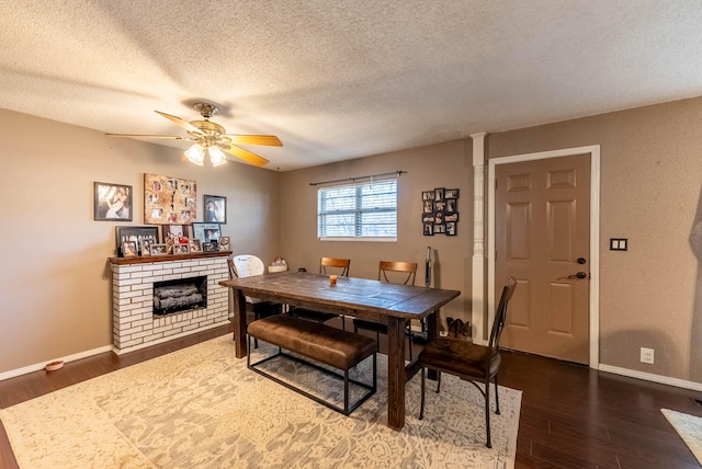 dining area with ceiling fan, a fireplace, dark wood-type flooring, and a textured ceiling