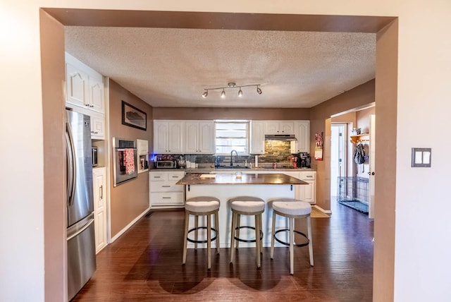 kitchen with white cabinetry, dark hardwood / wood-style flooring, a breakfast bar, a kitchen island, and appliances with stainless steel finishes