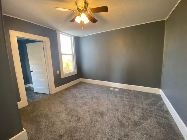 unfurnished room with ceiling fan, ornamental molding, and dark colored carpet