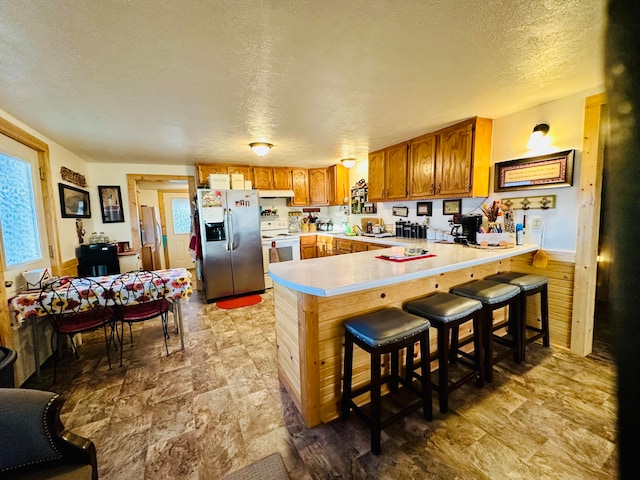 kitchen with a kitchen breakfast bar, kitchen peninsula, a textured ceiling, white electric range oven, and stainless steel fridge with ice dispenser