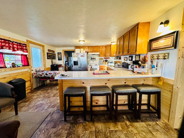 kitchen featuring dark wood-type flooring, stainless steel fridge with ice dispenser, white electric stove, kitchen peninsula, and wooden walls