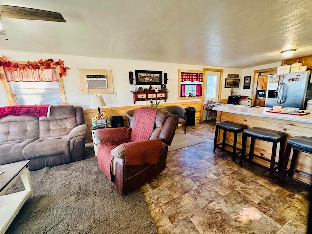 living room featuring an AC wall unit, wooden walls, ceiling fan, and a textured ceiling