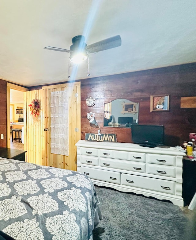 carpeted bedroom with ceiling fan and wood walls