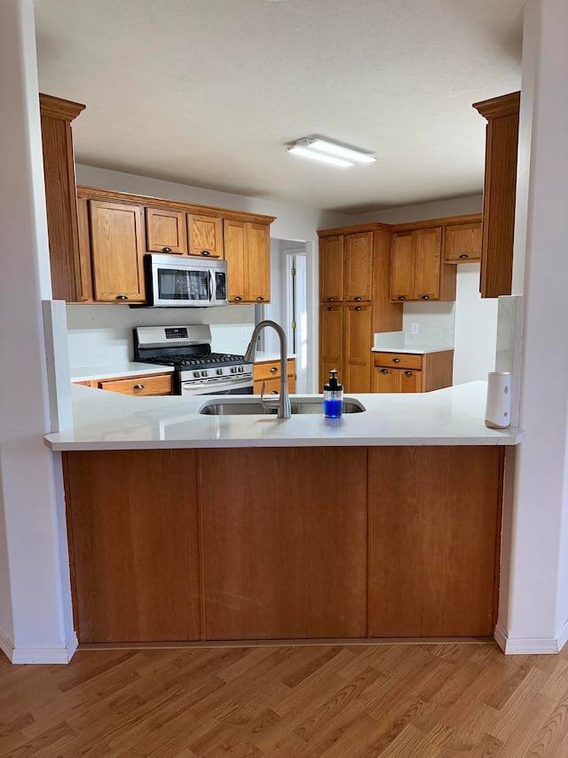 kitchen featuring kitchen peninsula, stainless steel appliances, light hardwood / wood-style flooring, and sink